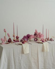 a table topped with lots of pink flowers and candles next to plates filled with desserts