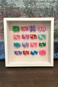 the letters are made out of colored plastic beads in a white shadow box on a wooden surface