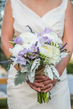 a bride holding a bouquet of white and purple flowers