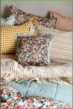 a bed covered in lots of pillows and blankets with colorful flowers on the pillow cases