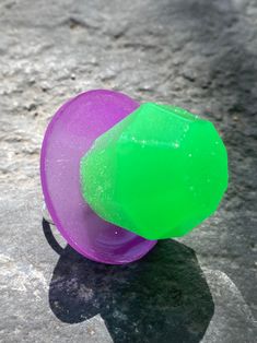 a purple and green object sitting on top of a cement ground next to a shadow