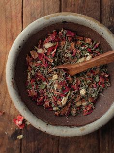 a wooden spoon is in a bowl filled with various types of flowers and herbs on a table