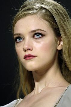 a woman with blue eyes and blonde hair is looking at the camera while wearing a silver dress