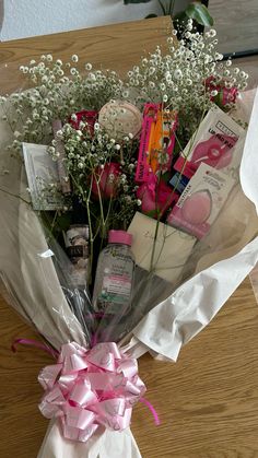 a bouquet of flowers wrapped in white paper with pink ribbon and some other items on the table