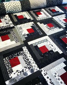 a black and white quilt on a bed with red and gray squares in the center