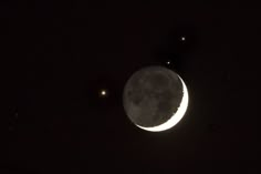 the moon is lit up in the dark night sky with three stars above it, and two small white dots on the right side of the moon