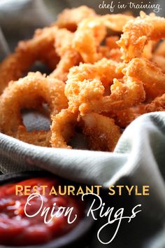 a basket filled with fried onion rings next to ketchup on a tablecloth