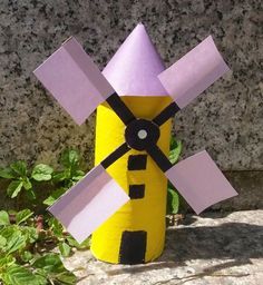 a paper mache made to look like a yellow and purple windmill sitting on top of a rock