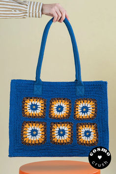 a blue crocheted bag with orange and white squares on it, sitting on top of a stool