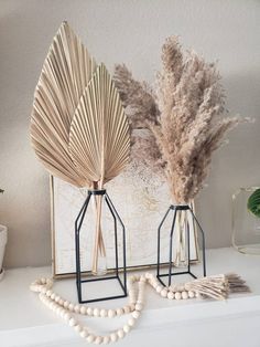 two decorative items are sitting on top of a mantle next to a plant and beaded necklace