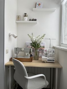 a desk with a chair, sewing machine and flowers in a vase on the table