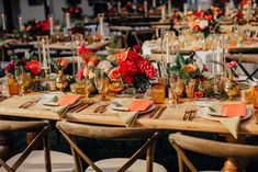 a table set up with orange and red flowers, candles and place settings for an event