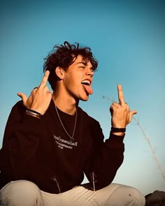 a young man sitting on the ground with his fingers in the air and making peace signs