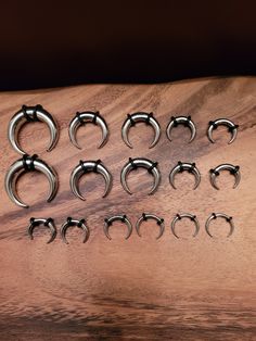 twelve pairs of stainless steel nose rings on a wooden surface with dark shadows in the background