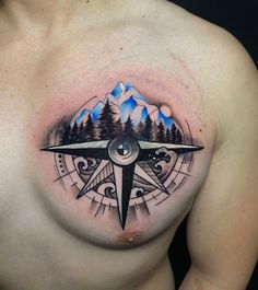 a man's chest with a compass tattoo on it and mountains in the background