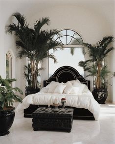 a large bed sitting in the middle of a room next to potted plants and a mirror