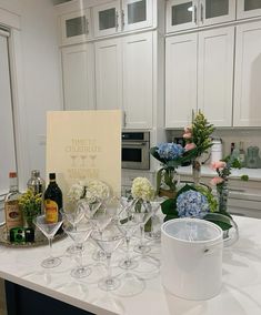 there are many wine glasses on the kitchen counter with flowers and bottles in front of them