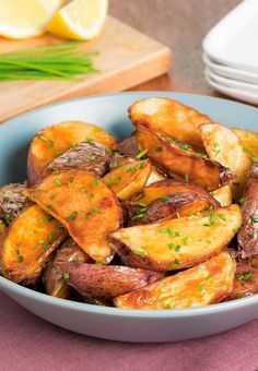 a blue bowl filled with cooked potatoes on top of a pink table cloth next to sliced lemons