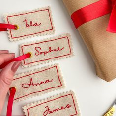 three tags with name written on them next to a wrapped present box and ribbon tied around it