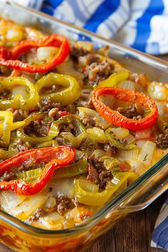 a casserole dish filled with meat, peppers and onions on a wooden table