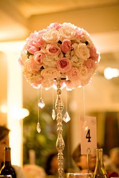 a tall vase filled with pink flowers next to bottles of wine and glasses on top of a table