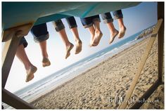 four people are hanging out on the beach with their feet in the air and one person is standing underneath them