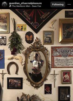 there is a wall with many pictures on it and a mirror in the middle that has a person's reflection