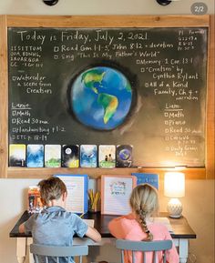 two children sitting at a desk in front of a blackboard with writing on it