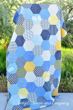 a blue and yellow patchwork quilt sitting on top of a cement slab in front of some trees