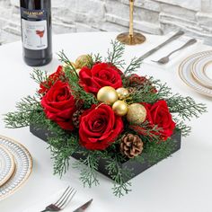 a christmas centerpiece with red roses, pine cones and gold baubles sits on a table