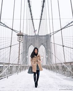 a woman walking across a bridge in the snow with her coat over her shoulders and boots on