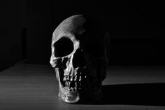 a black and white photo of a human skull on a wooden table in the dark