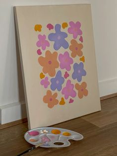 an easel sitting on the floor next to a painting with flowers painted on it