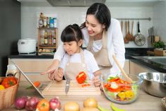 a mother and daughter preparing food together in the kitchen with chopsticks on cutting board