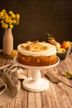 a cake sitting on top of a white cake plate next to flowers and fruit in a vase