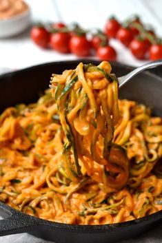 a fork full of noodles with tomatoes in the background