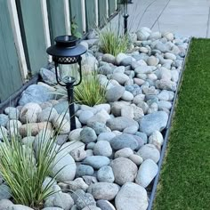 a garden with rocks and grass next to a fenced in area that has a lamp on it