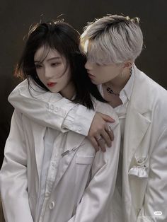 two young people are hugging each other in front of a black wall and one is wearing a white coat