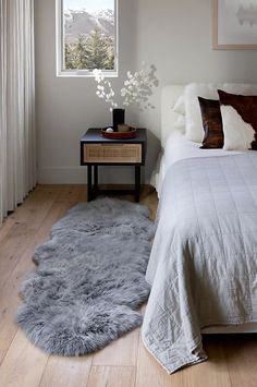 a bedroom with a bed, nightstand and black sheepskin rug on the wooden floor