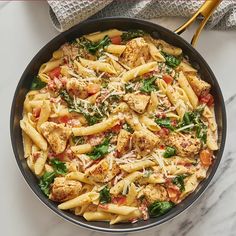 a skillet filled with pasta, chicken and spinach on top of a marble counter