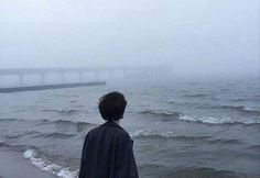 a man standing on top of a beach next to the ocean with a bridge in the background