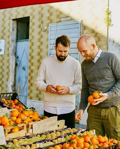 two men are looking at oranges on display