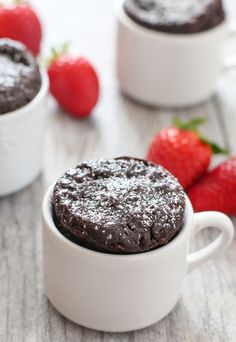 two mug cakes with chocolate frosting and strawberries in the background on a table