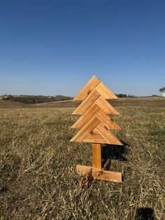 a small wooden christmas tree in the middle of a field with blue sky and grass