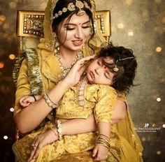 a woman holding a small child in her arms while she is dressed in yellow and gold