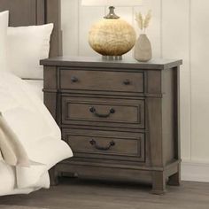 a night stand with two drawers and a lamp on it next to a white bed