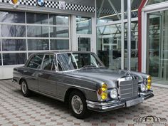 an old mercedes is parked in front of a car dealership with checkered flooring