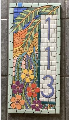 a mosaic tile wall hanging on the side of a building with flowers and leaves painted on it