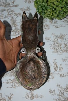 a person holding an old metal object in their left hand on a table with a wallpaper