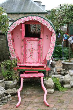 a pink and green carriage sitting in the middle of a garden with potted plants